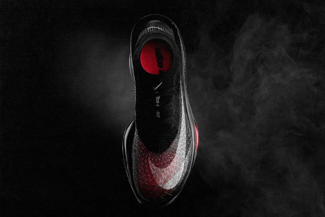Vista desde arriba de la Nike Apex negra sobre fondo oscuro, con el Flyknit en degradé de gris a rojo, el Swoosh blanco y el interior rojo sin plantilla