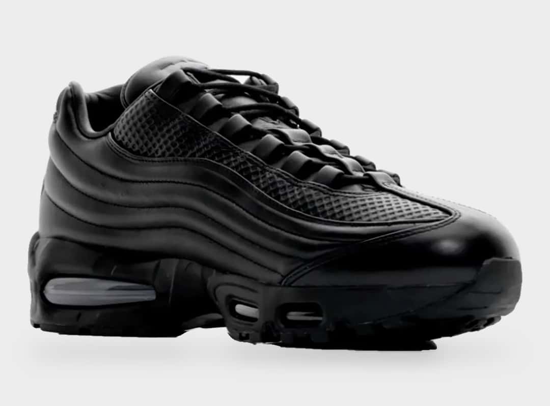 Nike Air Max 95 Lux de One Block Down de perfil sobre fondo gris claro, con cuero negro en las capas laterales, la zona de la puntera con textura cuadriculada y la cámara Air visible en el antepié y el talón