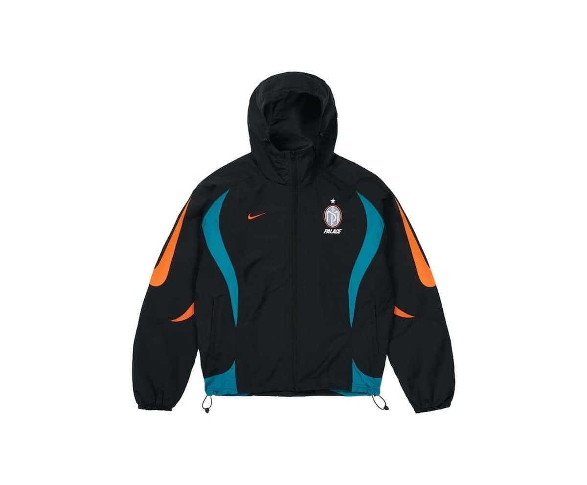Campera negra de la colección Palace x Nike Manor Place FC sobre fondo blanco, con paneles verde azulado y naranja, el Swoosh naranja y el escudo de Manor Place en el pecho