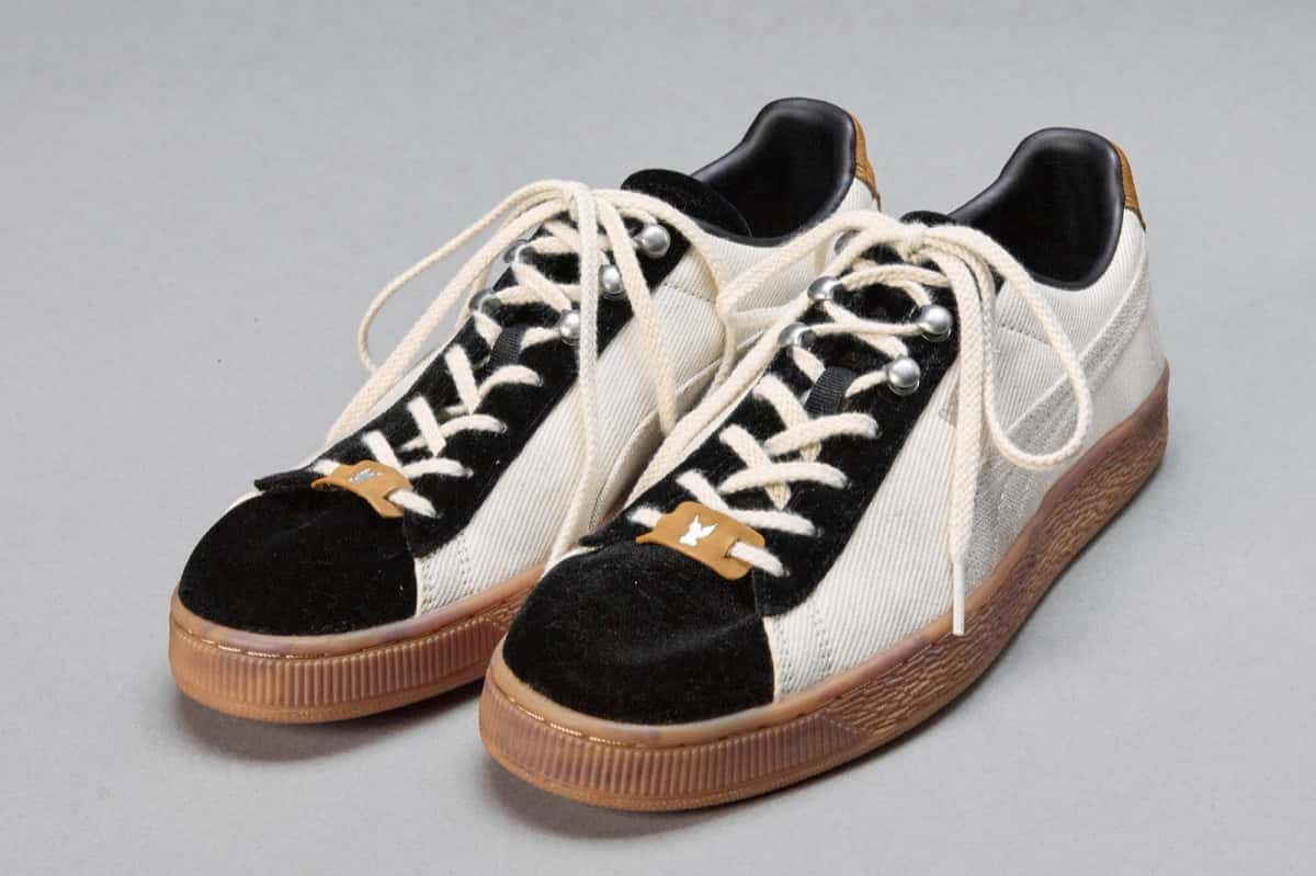 Par de PUMA x MASU Curio Suede Ivory x Black sobre fondo gris, con cuerpo marfil, puntera y zona de cordones en gamuza negra, ganchos plateados, cordones crudos, etiqueta marrón en los cordones y suela de goma color caramelo