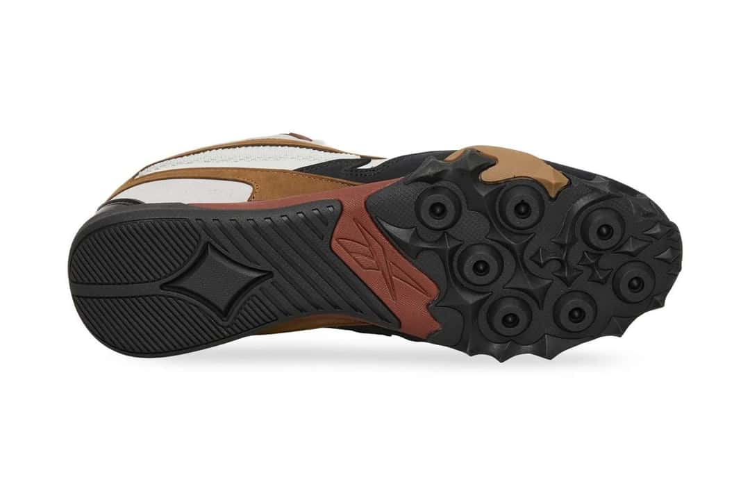 Suela de la Reebok Spike Racer vista desde abajo, con los tacos redondos en la punta, el dibujo de diamante y el logo de Reebok