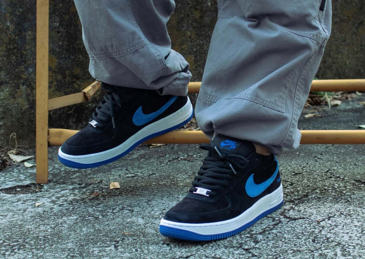 Nike SB Air Force 1 de Instant puestas sobre el asfalto, con upper de gamuza negra, Swoosh de gamuza azul, mediasuela blanca y suela azul
