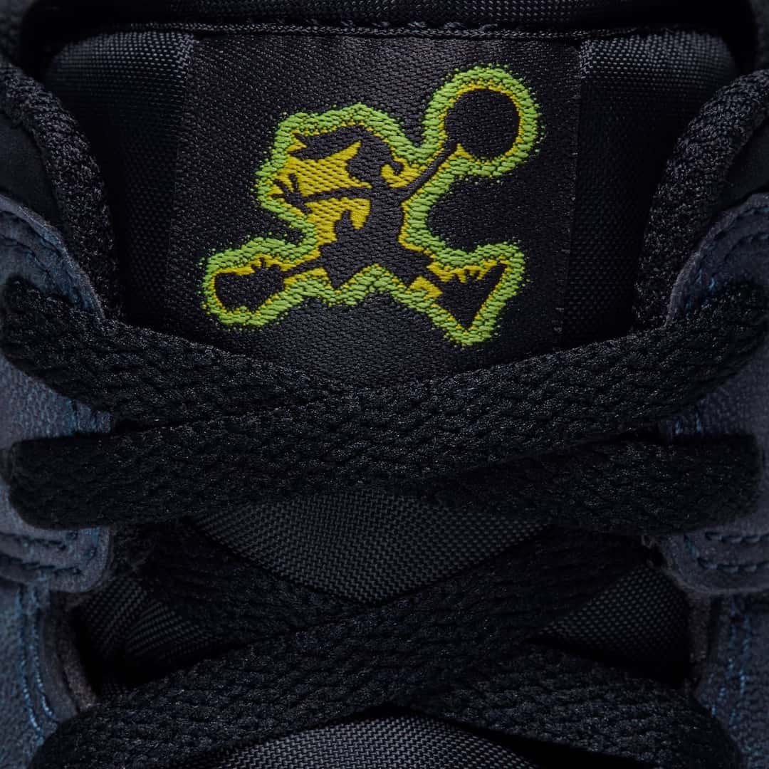 Primer plano de la lengüeta negra del Air Jordan 1 Mid SE de Space Jam con el logo de Bugs Bunny en pose de Jumpman bordado en amarillo con contorno verde, y los cordones negros cruzados adelante