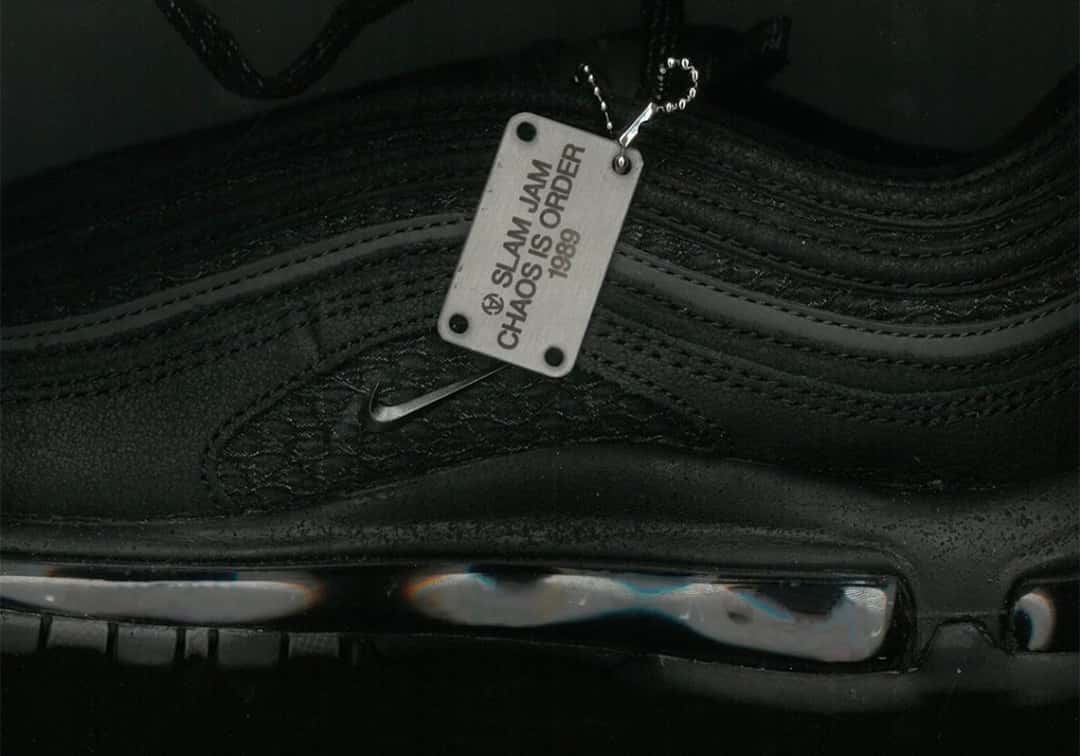 Detalle lateral de la Slam Jam x Nike Air Max 97 negra, con el Swoosh chico de metal y la placa plateada con la inscripción Slam Jam Chaos Is Order 1989
