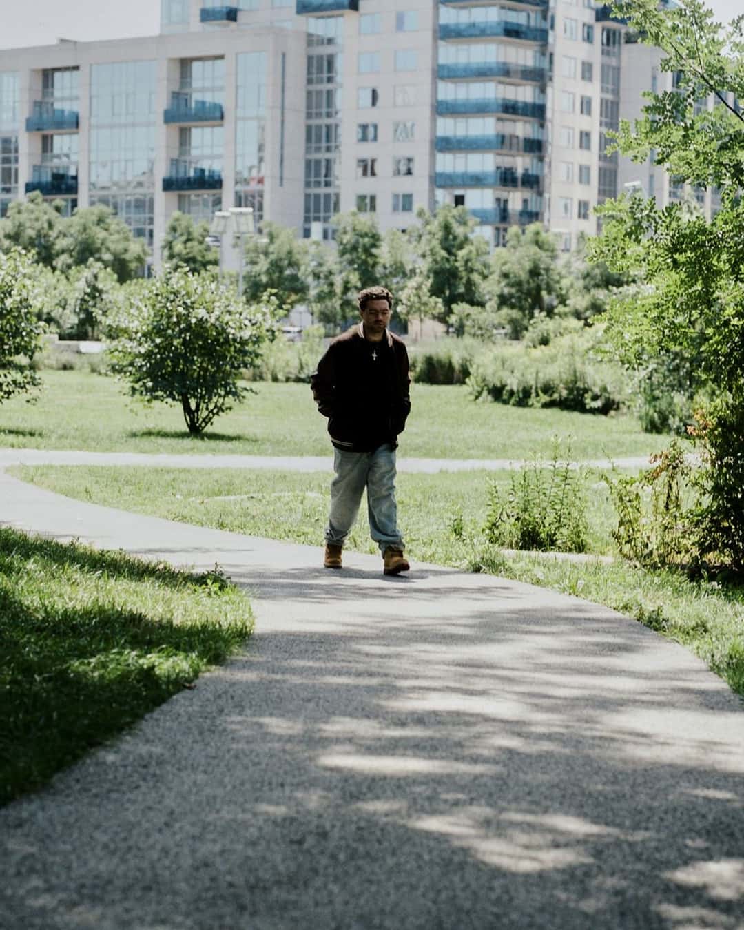 Hombre caminando por un sendero de parque con botas Timberland de Slam Jam y pantalón claro
