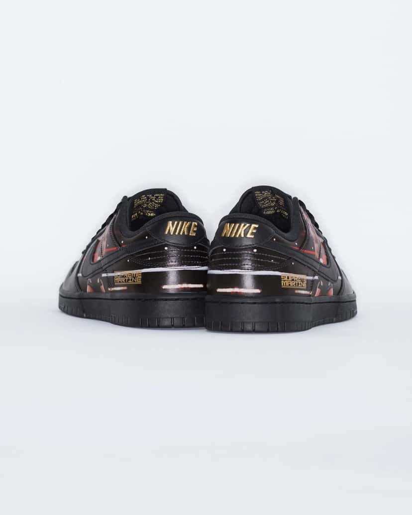 Vista trasera del par del Supreme x Martine Rose x Nike Dunk Low Tyson sobre fondo blanco, con la palabra Nike en dorado en cada talón, la placa dorada Supreme Martine y parte de la foto del ring en negro, rojo y blanco