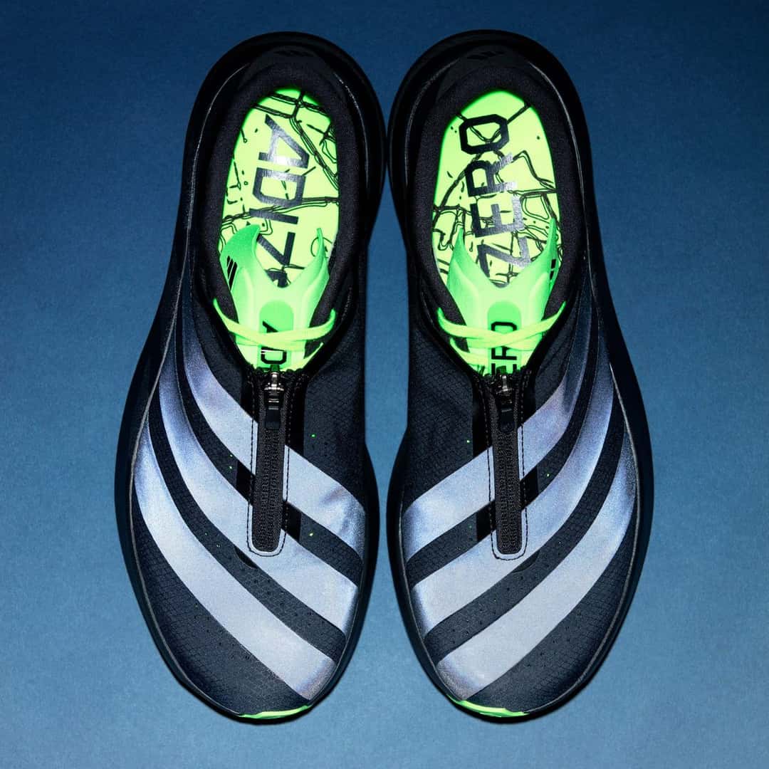 Vista desde arriba del par de Sneakersnstuff x adidas Adizero Evo SL Zip con las tres tiras reflectivas encendidas, el cierre al medio y las plantillas verdes con un mapa de calles