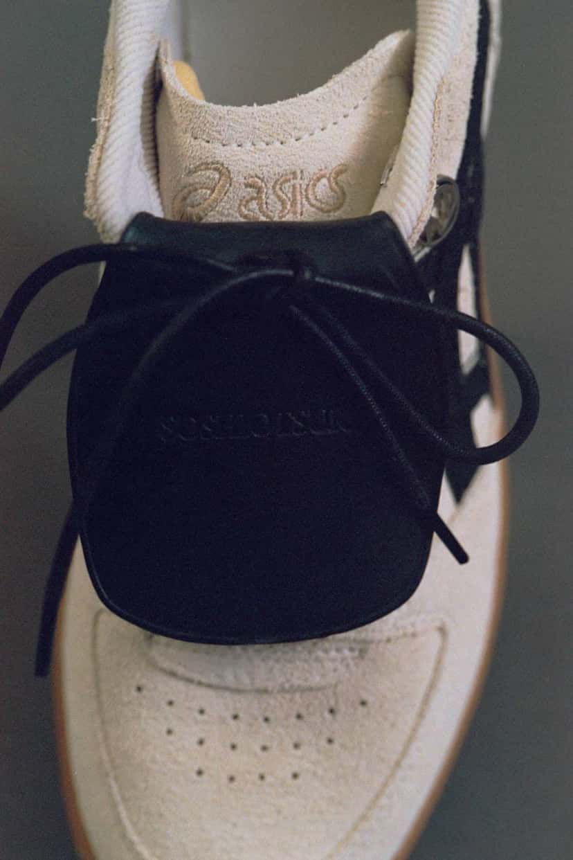 Detalle de la lengüeta grande de cuero negro con el nombre de SOSHIOTSUKI grabado, sobre la gamuza crema de la ASICS Skyhand OG