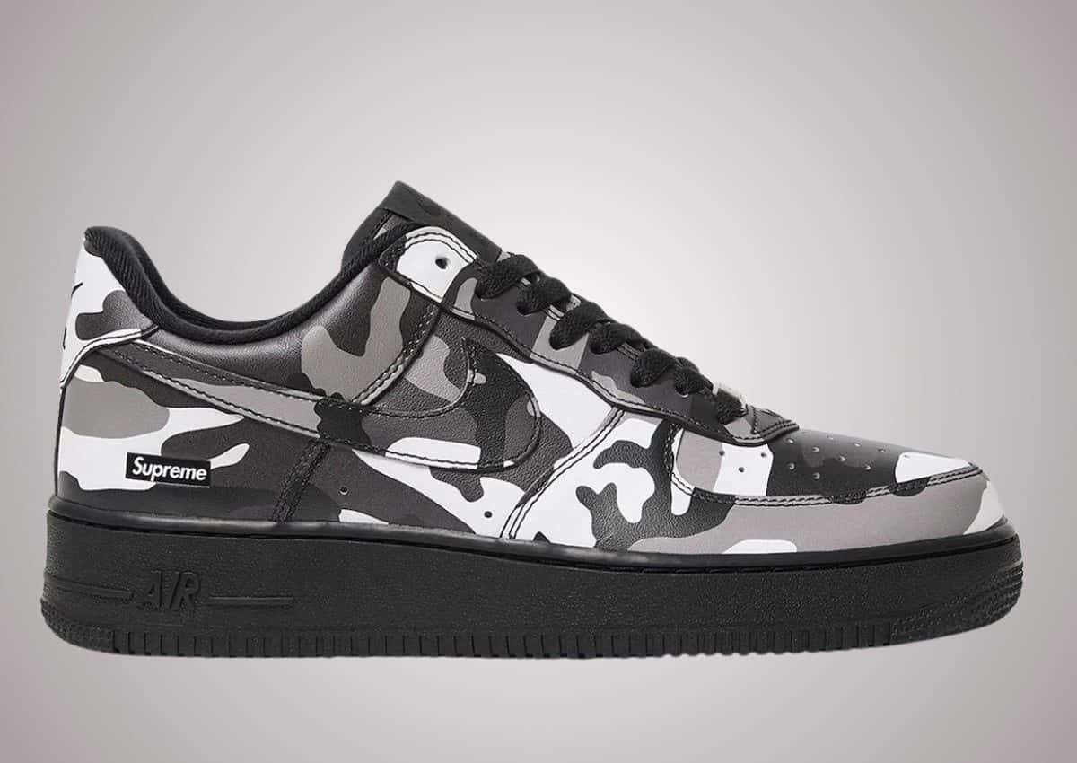 Supreme x Nike Air Force 1 Low Snow Camo de perfil, con camuflaje blanco, gris y negro en la capellada, el box logo de Supreme en el talón y la suela negra