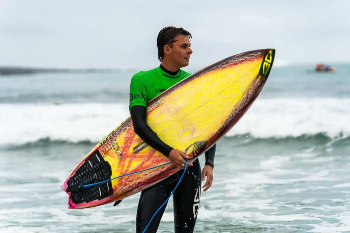 Un surfista con la lycra verde del EDP Ericeira Pro sale del agua con su tabla amarilla en Ribeira d'Ilhas