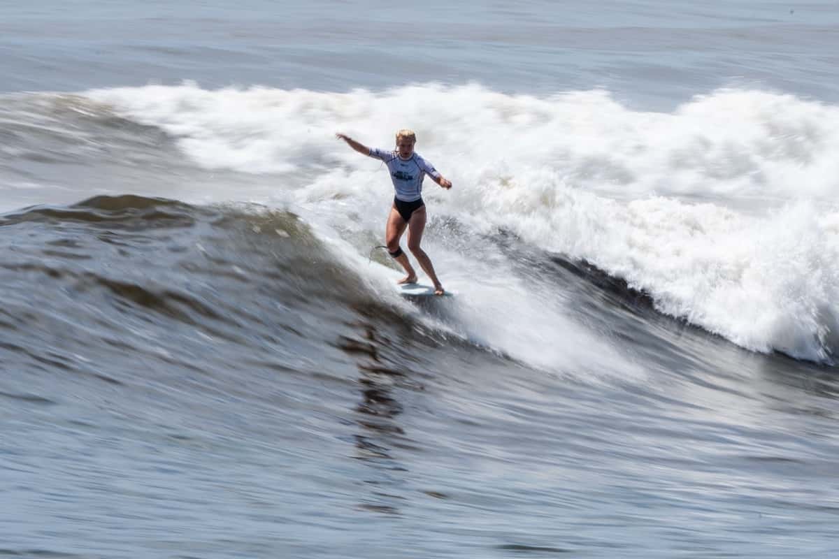 Thilde Rasmussen, con lycra blanca, camina sobre su longboard con los brazos abiertos en una ola de El Sunzal, con la espuma detrás