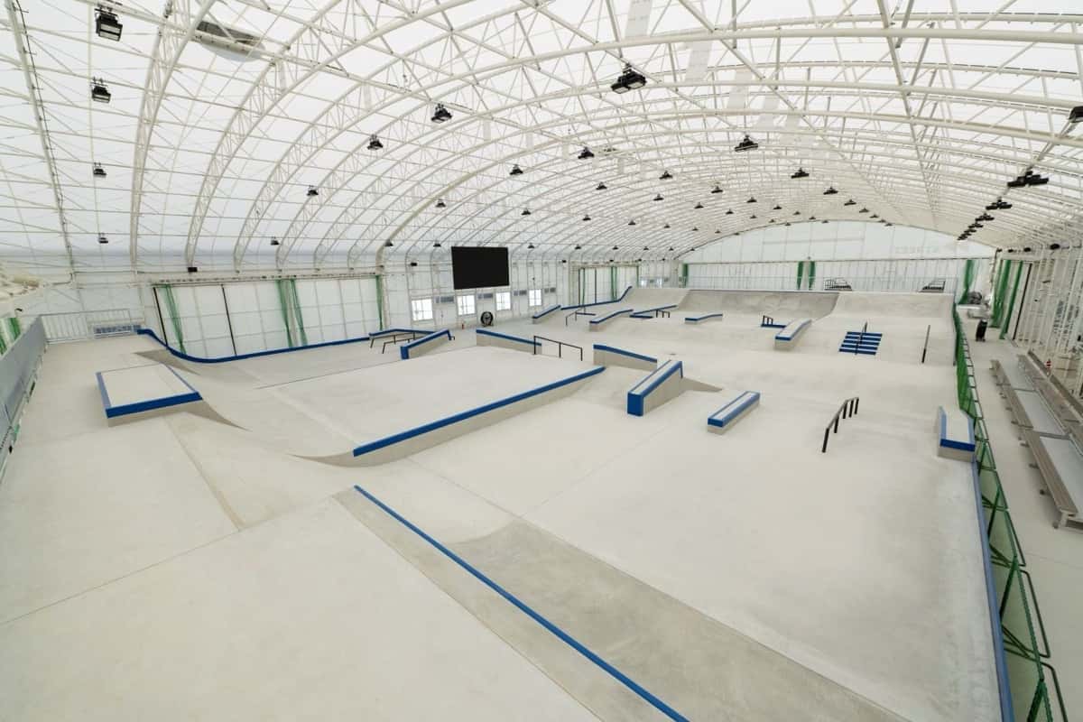 La pista de street del Tenjin Street Park de Fukuoka, bajo un techo de arcos blancos, con cajones de bordes azules, barandas, escaleras y una pantalla gigante al fondo