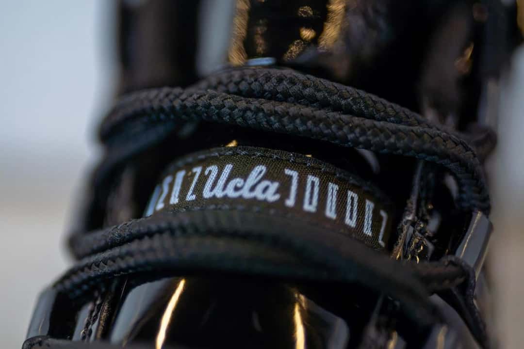 Lengüeta del botín Air Jordan 11 Gammas de UCLA, con el logo de UCLA en letra cursiva repetido sobre una cinta negra
