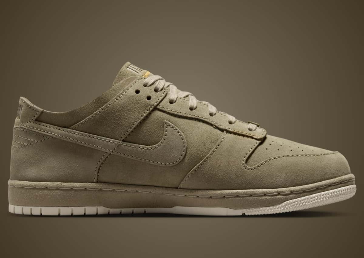 Union x Nike Dunk Low Natural Selection en gamuza verde oliva, de perfil sobre fondo marrón