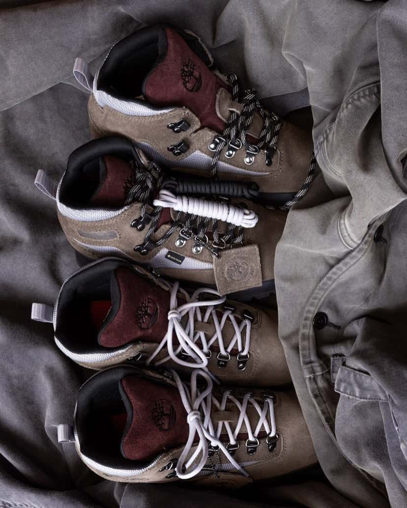 Cuatro botas Victor Kan x Timberland Euro Hiker apoyadas sobre tela gris, en gamuza taupe con lengüeta bordó, malla gris clara y la etiqueta Gore-Tex en el lateral, dos con cordones gris claro y dos con cordones negros con blanco, más un juego de cordones extra enrollado