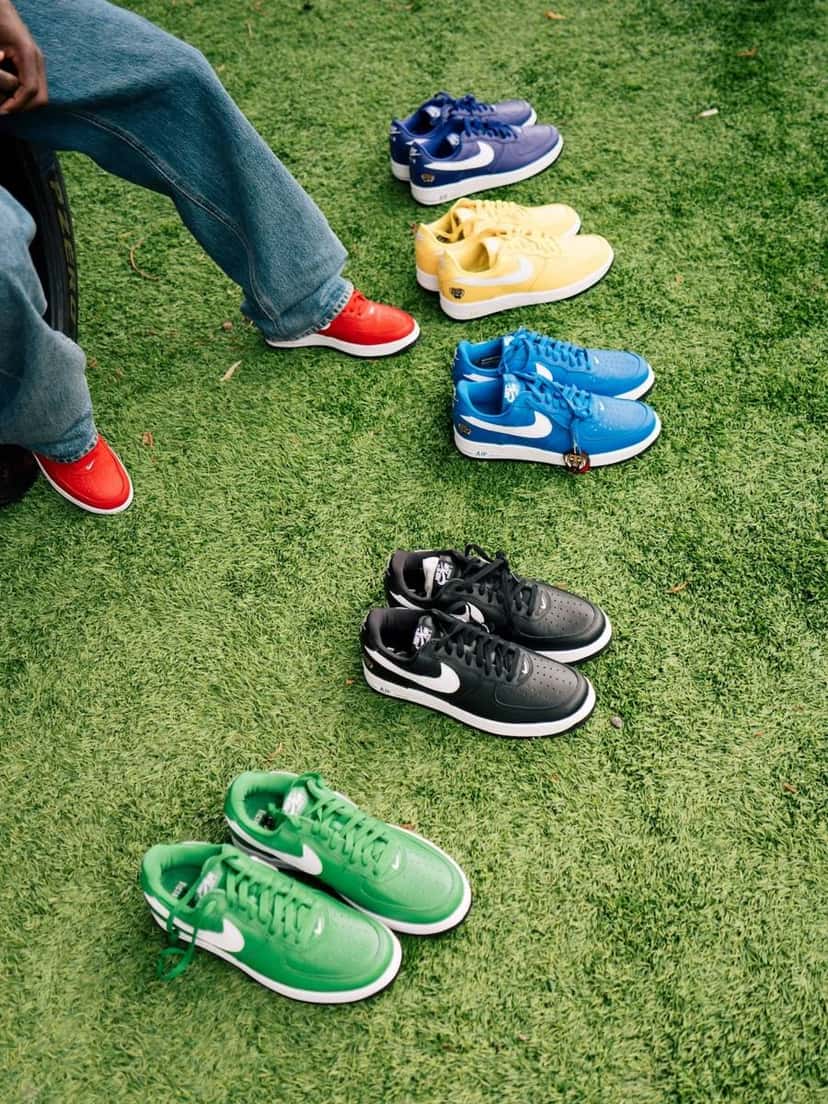 La colección de Air Force 1 '01 de Victor Victor apoyada sobre el pasto: pares en azul, amarillo, negro y verde junto a las zapatillas de una persona sentada