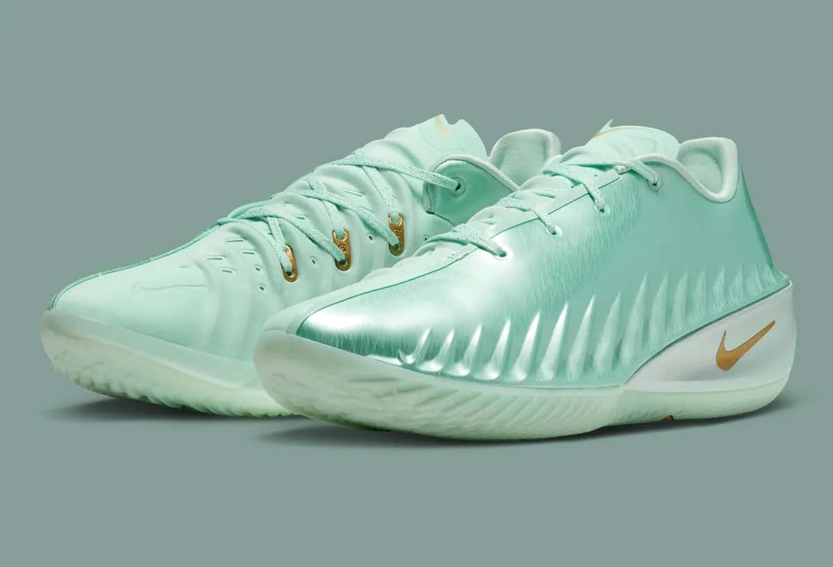 Par de Nike GT Cut 4 Statue of Liberty de Victor Wembanyama sobre fondo verde grisáceo, con upper verde menta metalizado, Swoosh dorado y ojales dorados