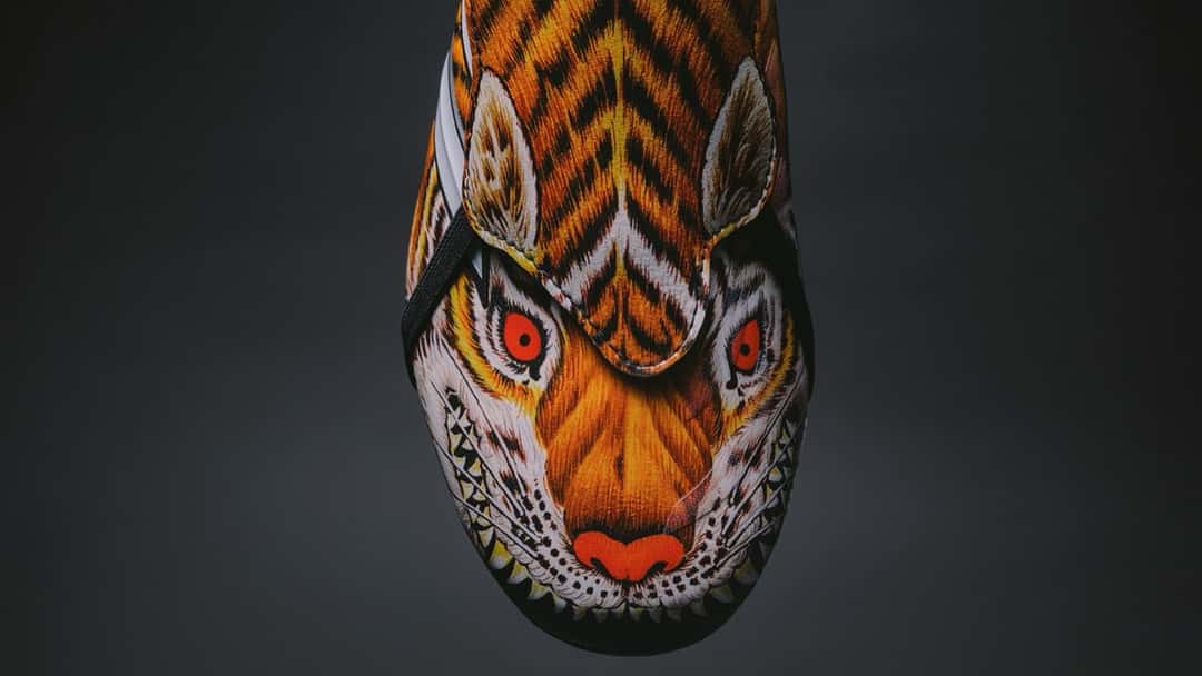 Puntera de la adidas Predator Y-3 con la cara de un tigre pintada en naranja, blanco y negro sobre fondo oscuro