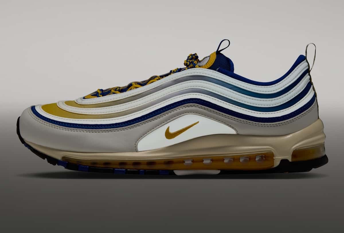 Nike Air Max 97 Yardrunners de North Carolina A&T de perfil, en blanco hueso con líneas azules y doradas y el Swoosh dorado