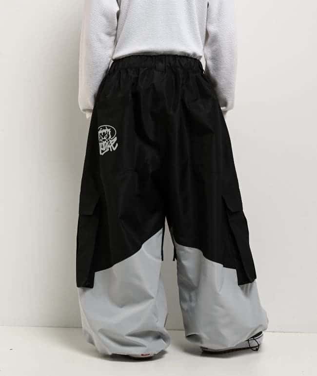 Vista trasera del pantalón de snowboard Empyre Tamarak ultra holgado, negro arriba y gris claro abajo, con bolsillos cargo laterales y un gráfico blanco en el bolsillo trasero